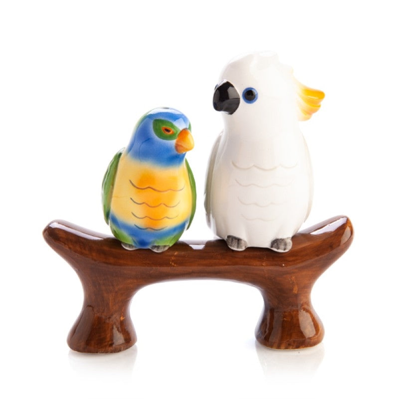 Two ceramic parrot figurines on a wooden branch against a white background